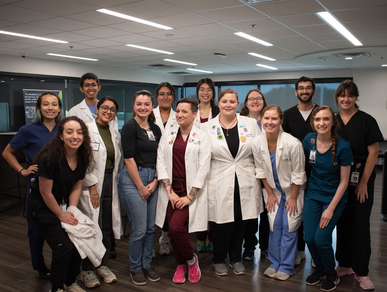 students in lab scrubs and white coats posing for a group photo