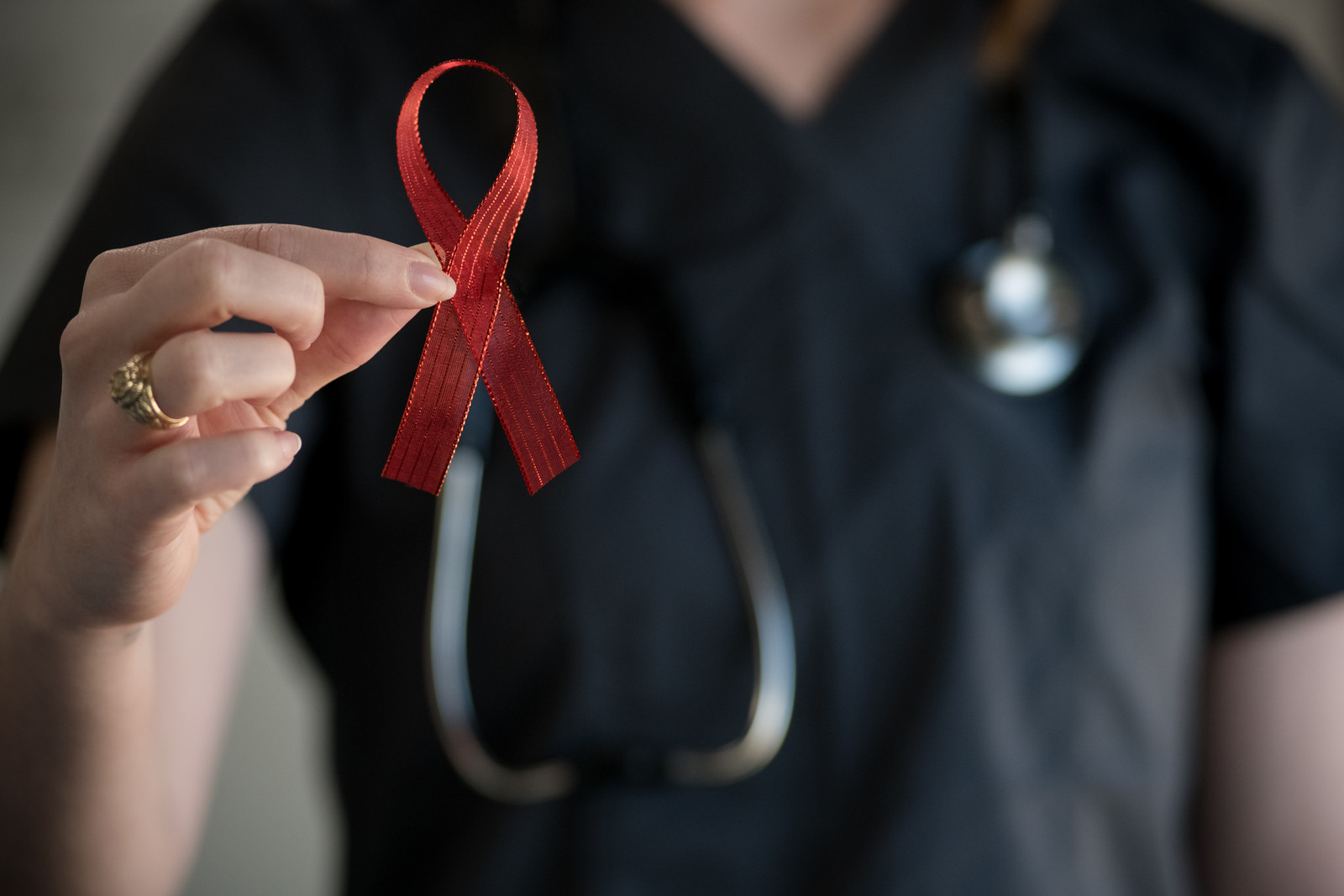 Person in scrubs with stethoscope holding up a red ribbon